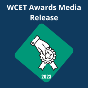 A digital graphic featuring a dark blue background with the text "WCET Awards Media Release" in bold white letters at the top. In the center, there is a green diamond shape containing a white line-art icon of a hand holding a star-shaped award ribbon. The year "2023" is written in white at the bottom point of the diamond.